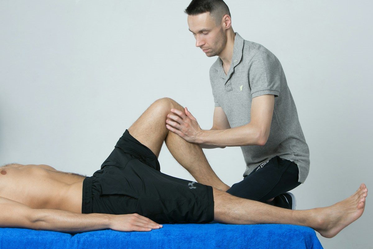 A physiotherapist examining a patient's bent knee on a treatment table