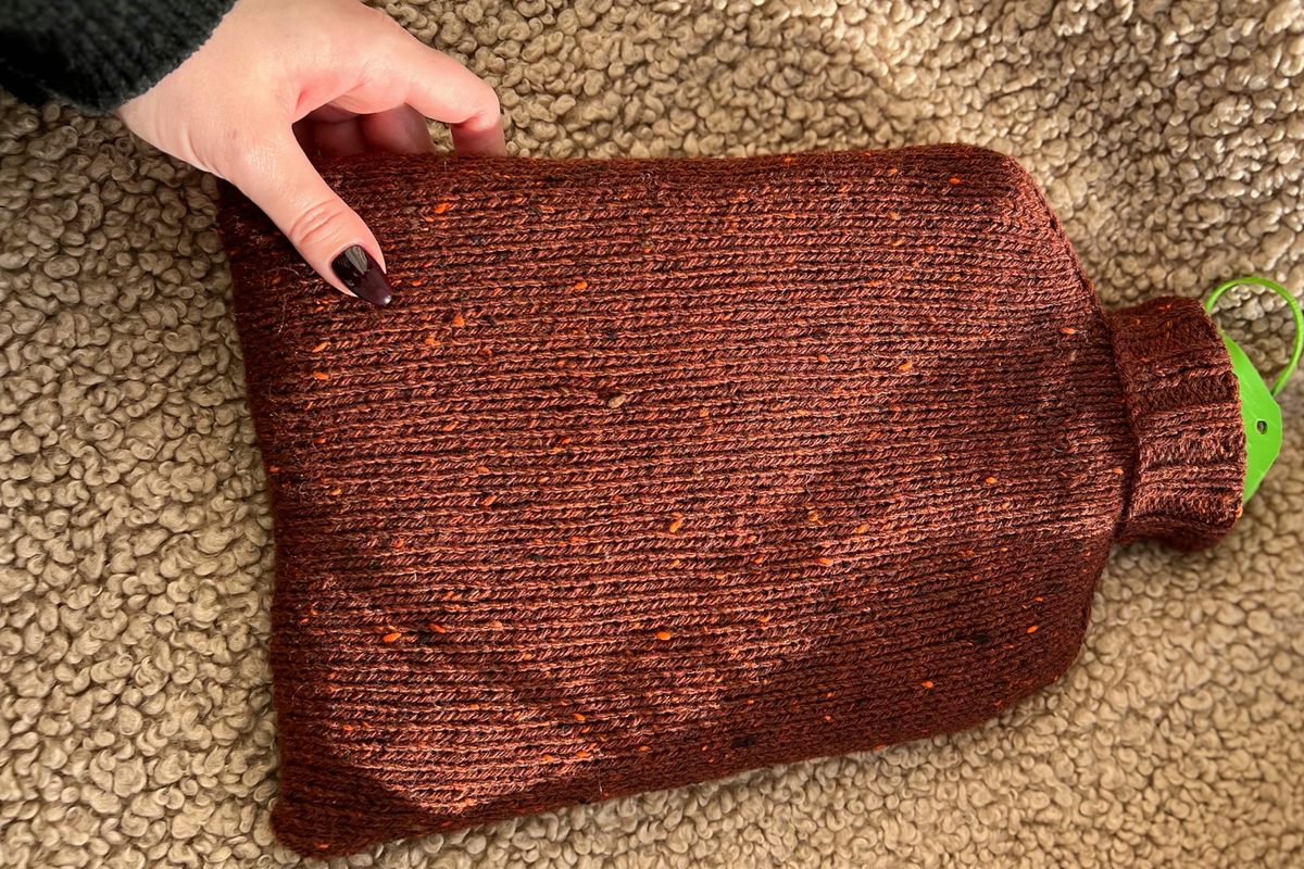 A hot-water bottle in a knitted cover on a soft blanket, ready to warm a stiff joint