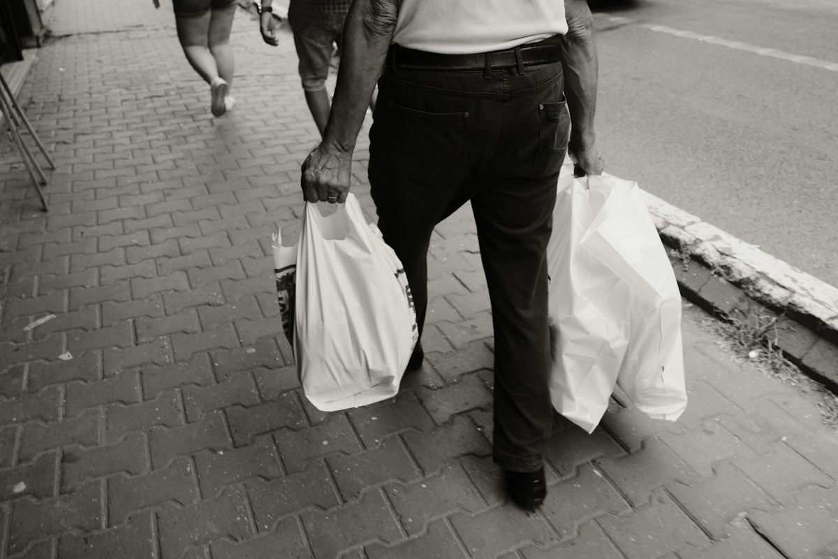 An older man walking with a heavy shopping bag in each hand, putting extra load on his hands, shoulders and knees