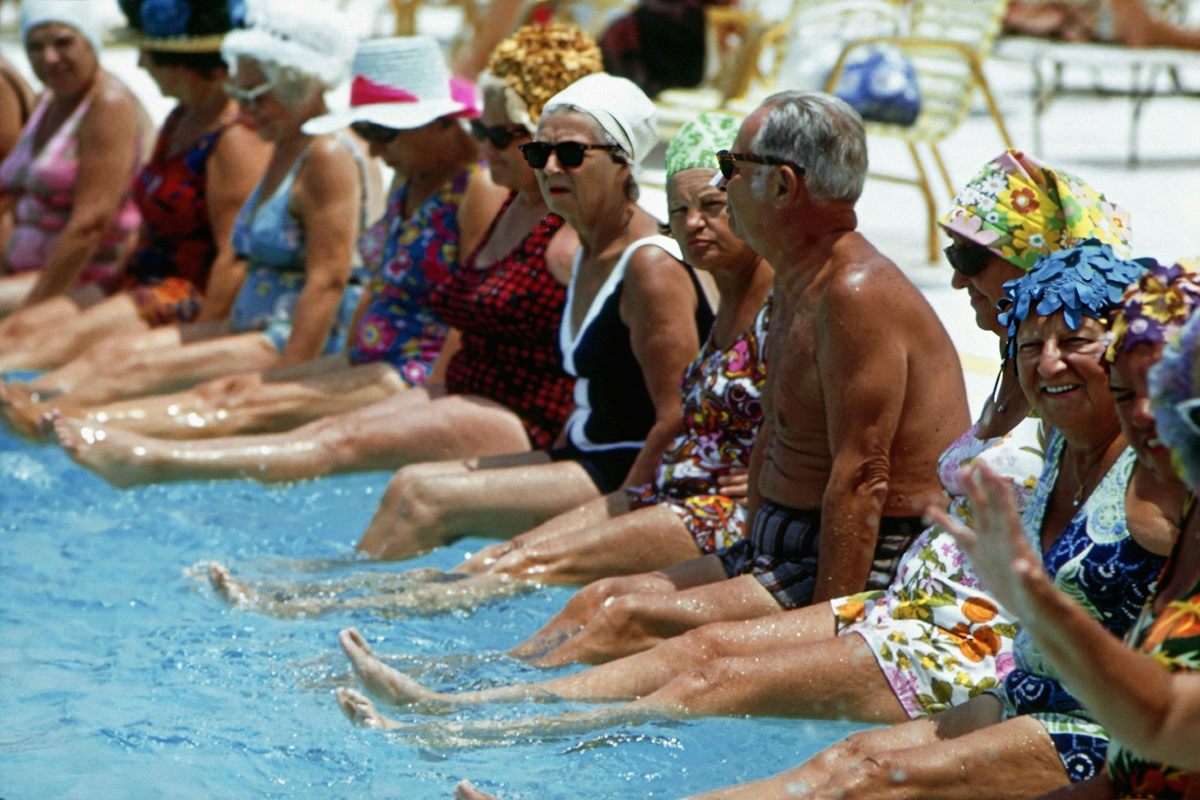 A group of older adults sitting on the edge of a pool and kicking their legs in the water