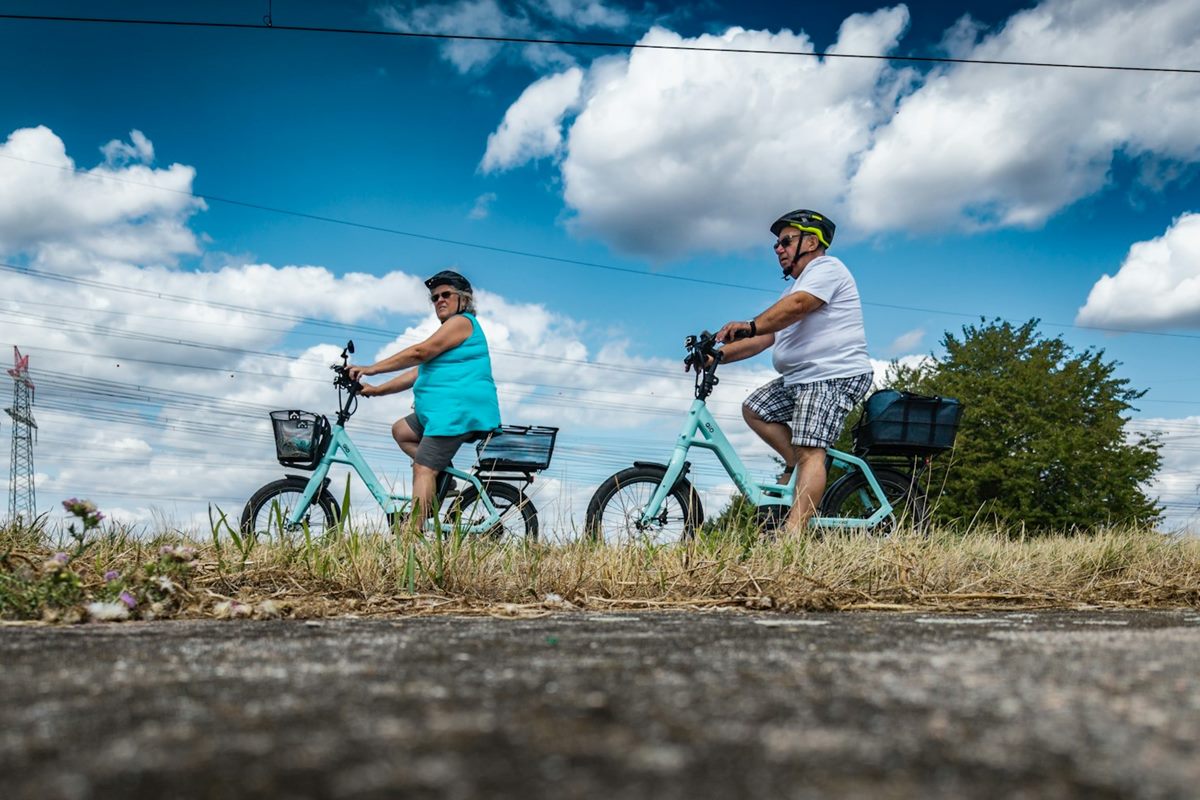 An older couple in helmets riding bicycles along a country path