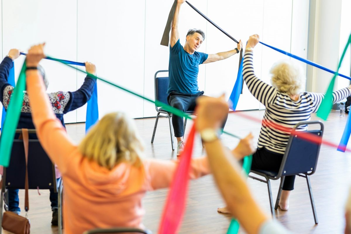 Older adults in a seated exercise class stretching resistance bands overhead